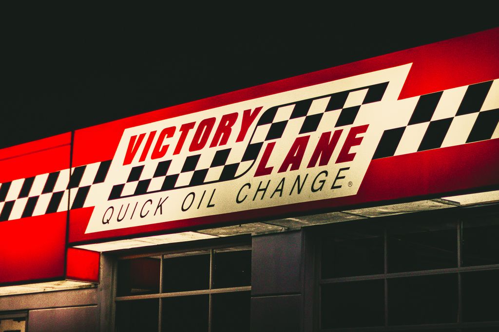 A vibrant sign for Victory Lane Quick Oil Change at night with checkerboard design.