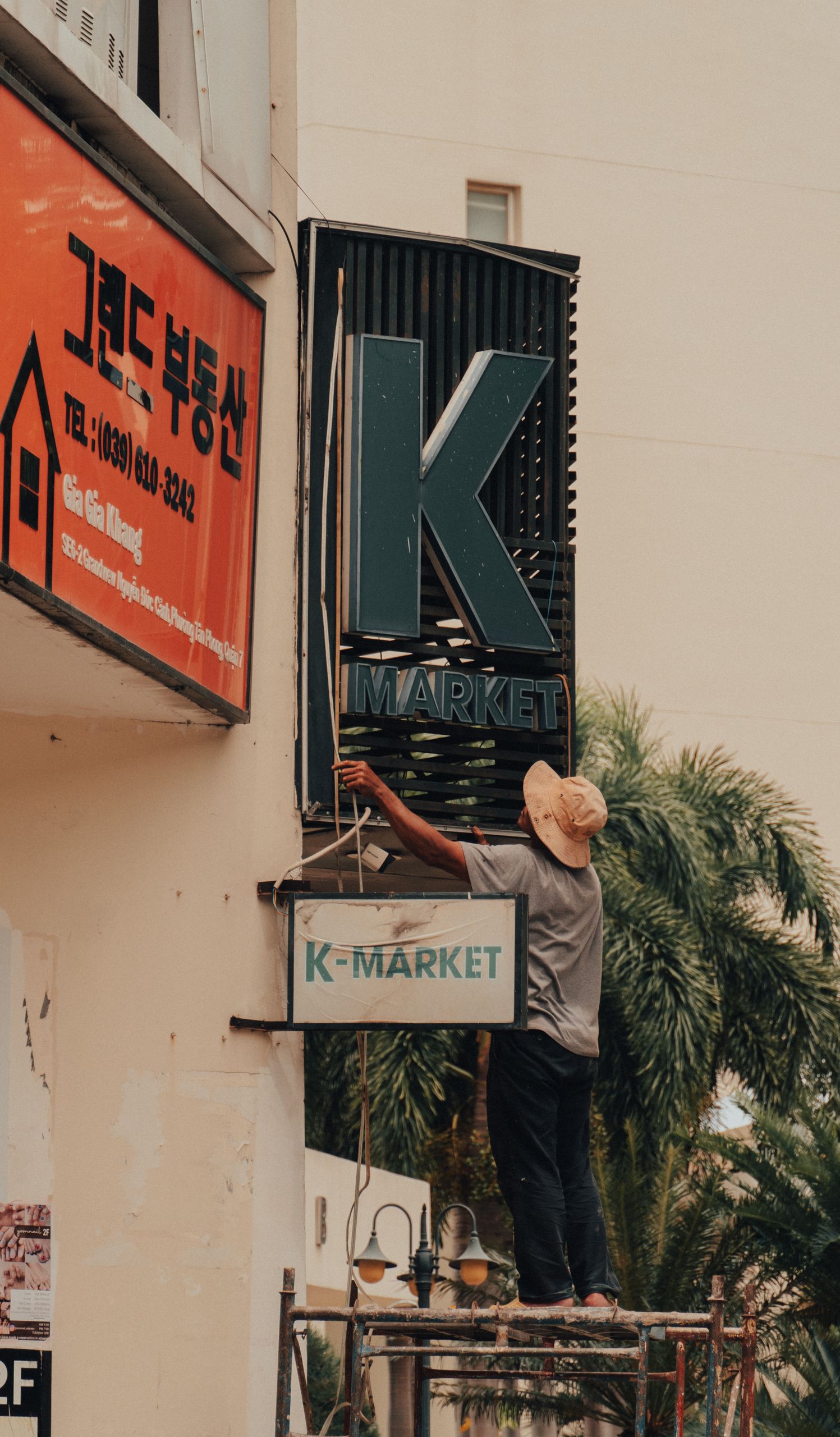 A worker fixing a K-Market sign on scaffolding beside a building facade.